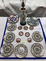 Full view of six large Imari style plates, four small round dishes, and a floral ceramic lamp on wooden base
