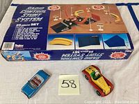Photo of the Radio Control Stunt System box with two toy cars placed in front of it, one red and yellow diecast with dog driver figure and one blue tin toy convertible car