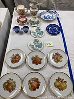 Photo showing a variety of transferware and Bavarian china including plates with fruit designs, blue and white plates with nautical patterns, cups, saucers, a pitcher, and creamer sets on a table.