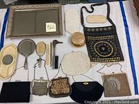Full view of vanity items including framed mirror, bags, comb, brushes, and powder box laid out on white cloth with blue tape edges.