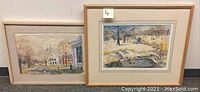 Two framed watercolor paintings side by side showing winter scene and town scene