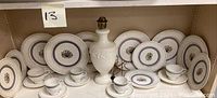 Full set of white Wedgwood Trentham china pieces with floral motif including bread plates, salad plates, cups, and saucers arranged on shelves with an embossed white ceramic lamp.