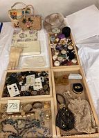 Photo showing multiple wooden trays containing assorted purses, sewing threads, buttons, jewelry, linens, and gloves on a white surface.