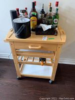 Front view of the wood bar cart with bottles and ice bucket on top, shows overall structure and wheels.