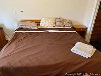 Full view of the wooden headboard attached to a bed with brown bedding, showing its width and height relative to the mattress and pillows.