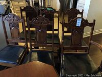 Front view of six wooden chairs showing carved backrests and black leather seats with scratches.