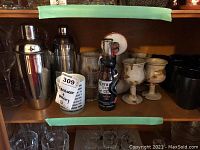 Middle shelf with cocktail shakers, martini glasses, pottery goblets, and bottle opener