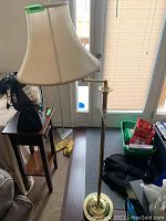 Brass floor lamp with beige fabric bell-shaped shade and pull chain switch