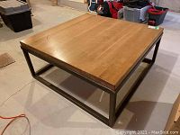 Full view of the modern square coffee table with wood top and metal base in a basement setting.