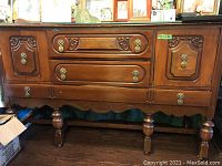 Front view of wooden sideboard showing two cabinet doors and three central drawers with decorative metal handles and carved panels.