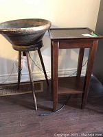 Full shot showing the wooden tripod stand with bowl-shaped top and the small wooden side table side by side against a wall.