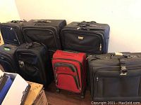 Seven suitcases arranged closely, showing various sizes and colors including black and red. Used condition visible.