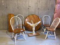 Photo of the entire set showing round wooden dining table top, two wooden leaves, four white-and-wood chairs in basement setting.