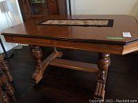 Photo of rectangular wooden table with carved legs and claw feet, octagonal tabletop with a decorative fabric runner showing floral embroidery placed in center.