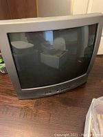 Front and angled front views of the vintage RCA box TV, showing the gray plastic housing and curved CRT screen.