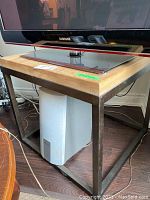 TV stand supporting a Samsung television, showing the wood top and metal frame base with some wear visible.