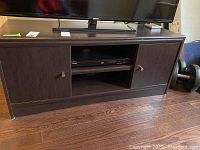 Front view of dark brown manufactured wood entertainment cabinet with two closed doors and central open shelf.