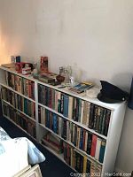 Full view of the white painted bookshelf filled with books and various small objects on top, showing scratches and wear.