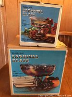 Photo showing two original boxes with images and descriptions of the carnival glass pieces inside, including the 5-inch Wedding Bowl and Garland Bowl by Indiana Glass Company.