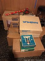 Boxes stacked including Nashua box, vintage Miller-Lites three candle light units box, and other plain and labeled boxes.