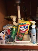 View of assorted cleaning products including Comet cleanser, SOS pads, and spray bottle under a sink.