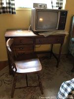 Four drawer wooden desk with chair beside it, showing overall wear and scratches.