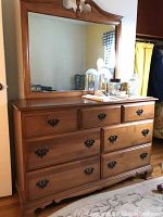Front angle showing the full dresser with seven drawers and matching mirror above; dresser has three small drawers in top row and four larger drawers below; mirror has decorative wooden top.