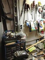 Hand tools displayed hanging on a pegboard with organized hardware boxes and green toolbox beneath.