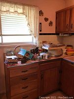 Overview of kitchen counter showing various kitchenware including vintage iron, metal canister, cake plate, cutting boards, and containers