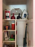 Shelf with Proctor Silex iron, red and black double-lamp lanterns, rolls of contact paper, handheld flashlights, and insulated container.