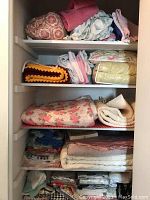 Shelves with assorted linens including Afghan, comforters, pillowcases, towels, blankets, and curtains