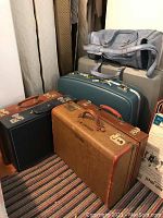 Photo showing four briefcases in front and two hard shell suitcases behind, plus a gray fabric carry-on bag on top