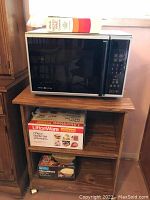 General Electric microwave oven on top of wooden rolling cart with microwave ovenware boxes on shelves below.