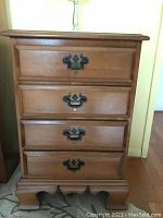 Front view of the wooden nightstand showing four drawers with metal handles and shaped base legs.