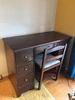 Front view of dark wood office desk with four drawers and a wooden chair with a padded blue patterned seat.