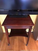 Front view of the wooden rolling table with television on top, showing tabletop and caster wheels.