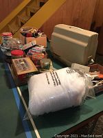 Full table view showing sewing machine case, tins, fabric, thread, and sewing notions spread out.