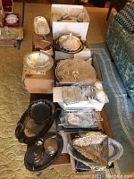 Wide view of various silverplate serving pieces, cranberry glassware, and Pyrex casserole dish arranged on a table and in boxes.