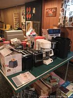 Overview of various small appliances on green table including toasters, coffee makers, shredder, and portable TV