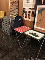 Four vintage metal TV trays folded and standing upright, two vintage aluminum webbed chairs behind them, and two metal folding chairs to the right.