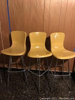 Three vintage yellow swivel bar stools with metal legs arranged side by side, showing full height and seat design.