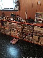 Wide view of a shelving unit filled with stacks of vintage magazines and small collectible items on top.