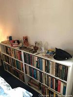 Shelf with vintage collectibles and books, including road maps, coin boxes, Avon cologne bottle, dark hat, and varied small items.