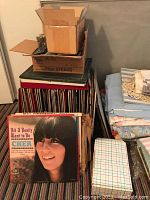 Photo showing stacks of vinyl records inside cardboard boxes, with Cher album cover visible in front.