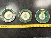 Three Arklow Pottery plates with detailed green and gold borders, each featuring a different Dublin family crest (Mallin, Dowling, Doyle). A tape measure shows their diameter around 5 inches.