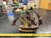 Side angle view of brass and copper ship sculpture on black metal surface with ruler for scale.