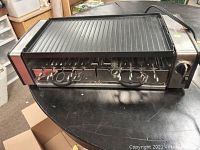 Front view of the Cuisinart electric hot dog and sausage grill showing six metal rotating skewers and ridged grill plate on top.