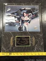 Frontal image of the marble memorial plaque showing race photo and dedication plate with measuring tape for scale.