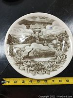 Top view of round decorative plate showing entire design including historical imagery and maple leaf border with beaver.