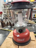 Front view of the red Coleman electric lantern showing the Coleman logo on the base and the clear glass light casing.